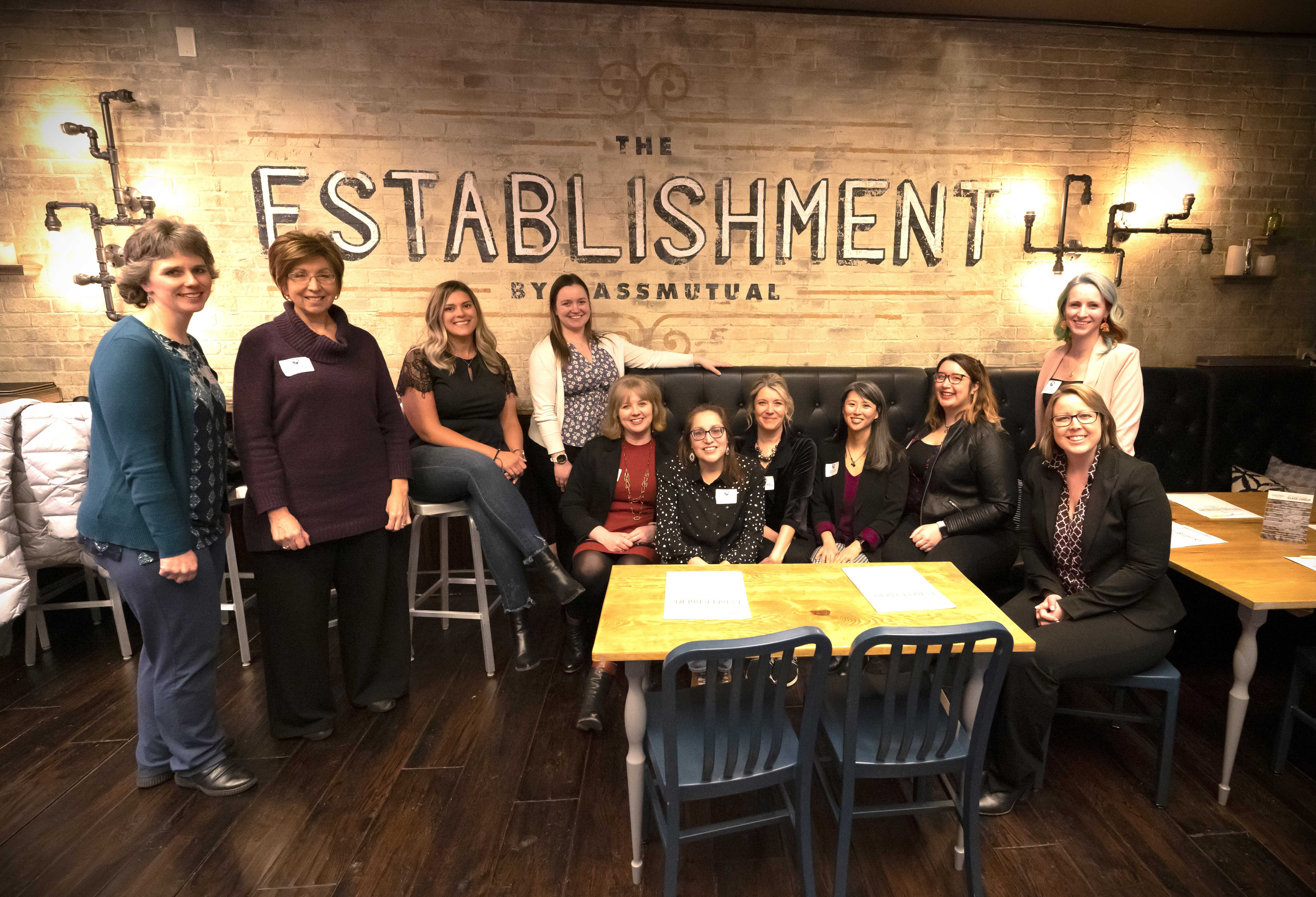 Group of 11 women seated in front of wall that says The Establishment