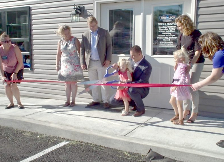 Little girl with dad cutting red ribbon at Load & Lock's ribbon cutting ceremony.