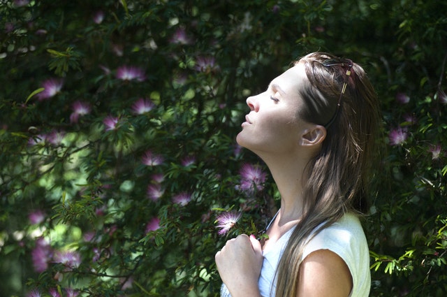 Woman taking in the sunlight next to a bush of purple flowers