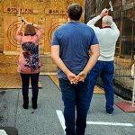 Woman axe throwing with gentlemen standing behind her