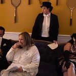 Guests sitting on couch and woman in top hat and tails behind them
