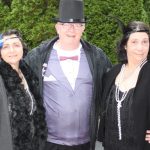 Two flapper women on either side of man with top hat and purple vest