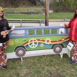 Two hippie women standing with hippie VW van prop