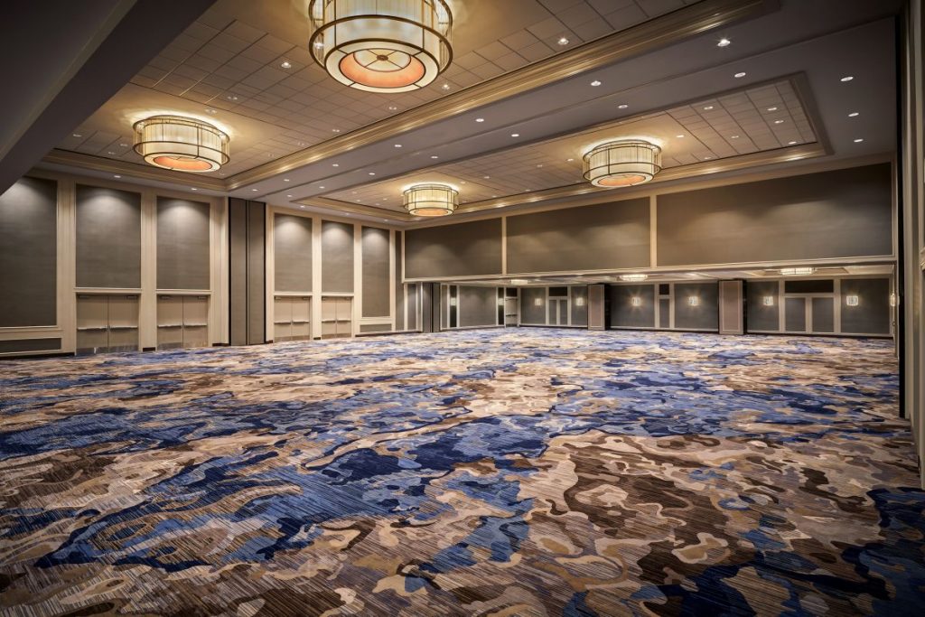 Mardi Gras Ballroom inside New Orleans Marriott. Blue, tan, and brown abstract water carpet, chandeliers, tan and cream colored walls.