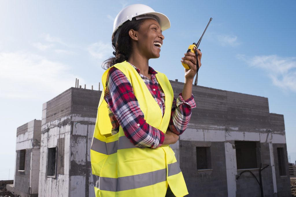 Constructor woman using walkie-talkie at construction site. Building contractor woman using walkie-talkie for communication.