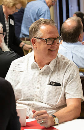 man smiling at someone at his table at luncheon