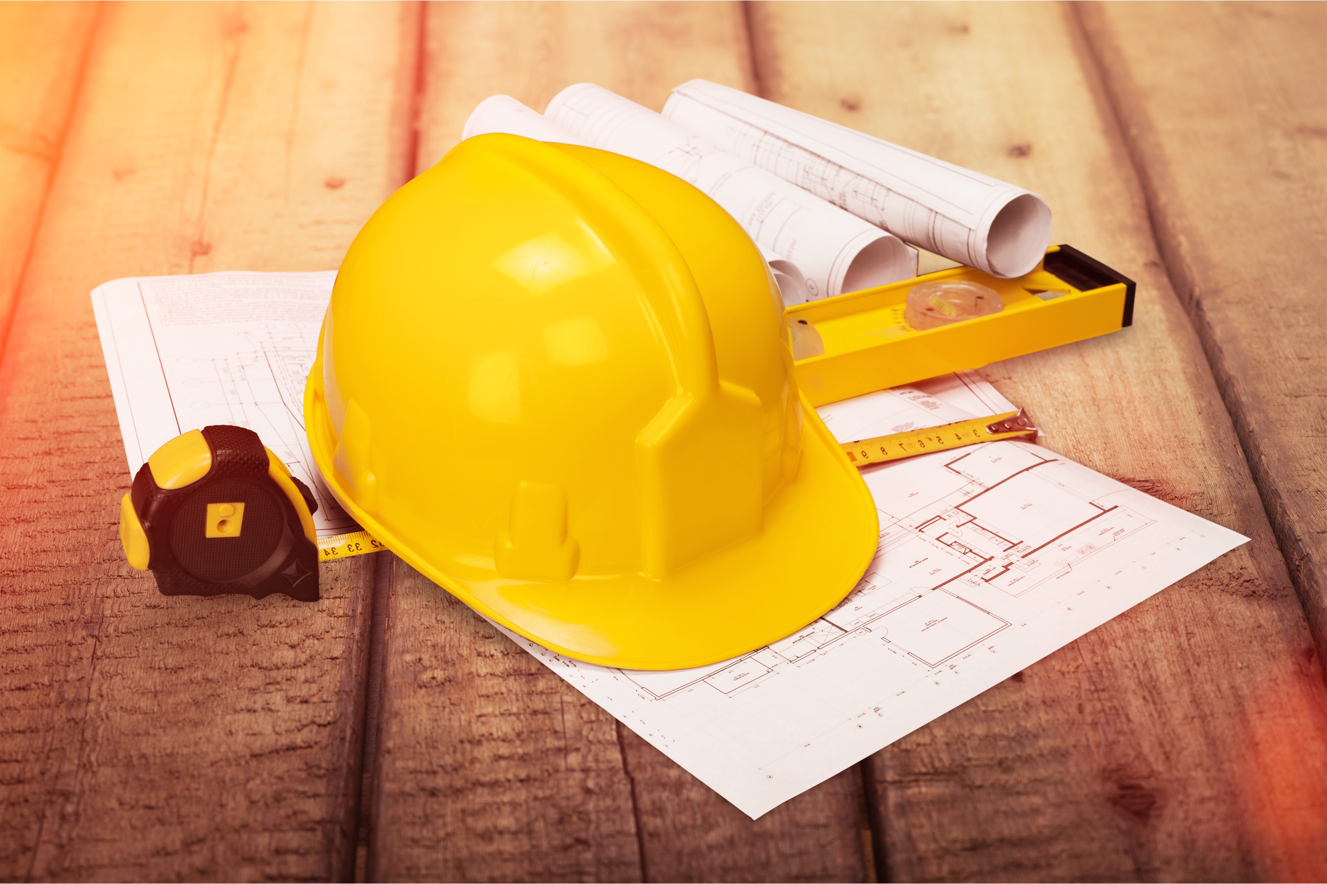 Yellow hard hat and blueprints on wooden desk in a construction concept