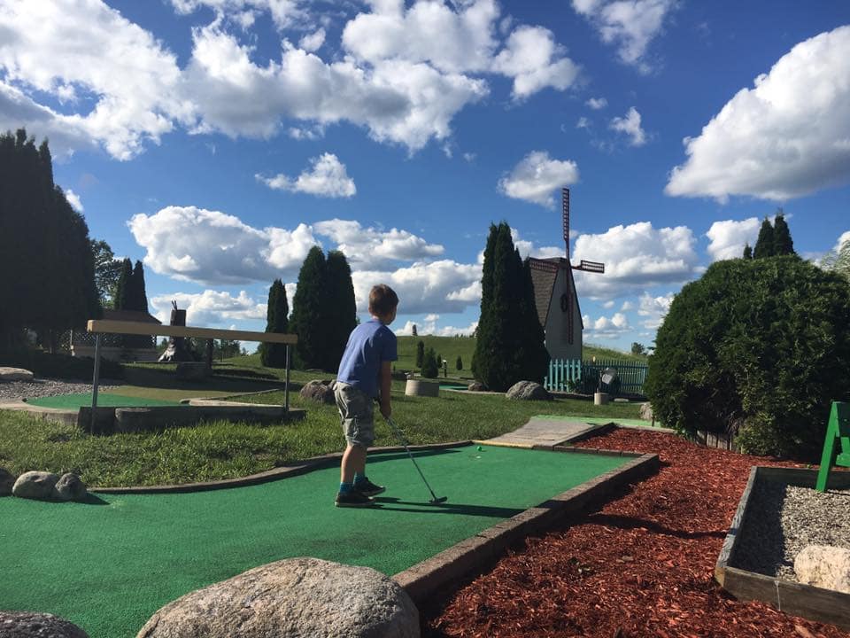 little kid playing putt putt golf on a sunny day