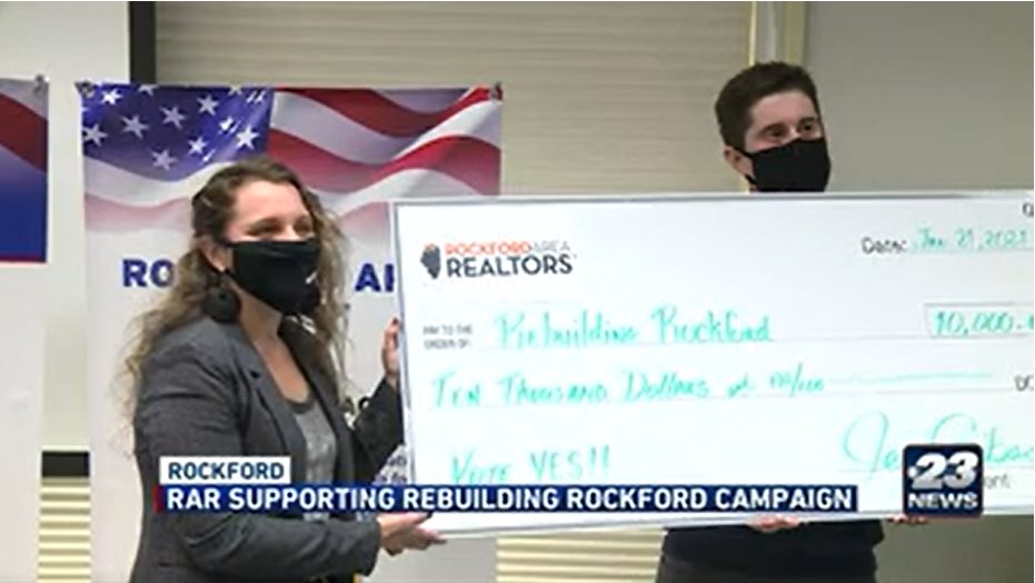 two people participating in check presentation. middle age female with gray blazer, facemask and long brown hair. middle age man with facemask and short black hair. Check for rebuilding rockford
