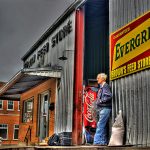 elderly man leaning against old metal building - Brown's Feed Store