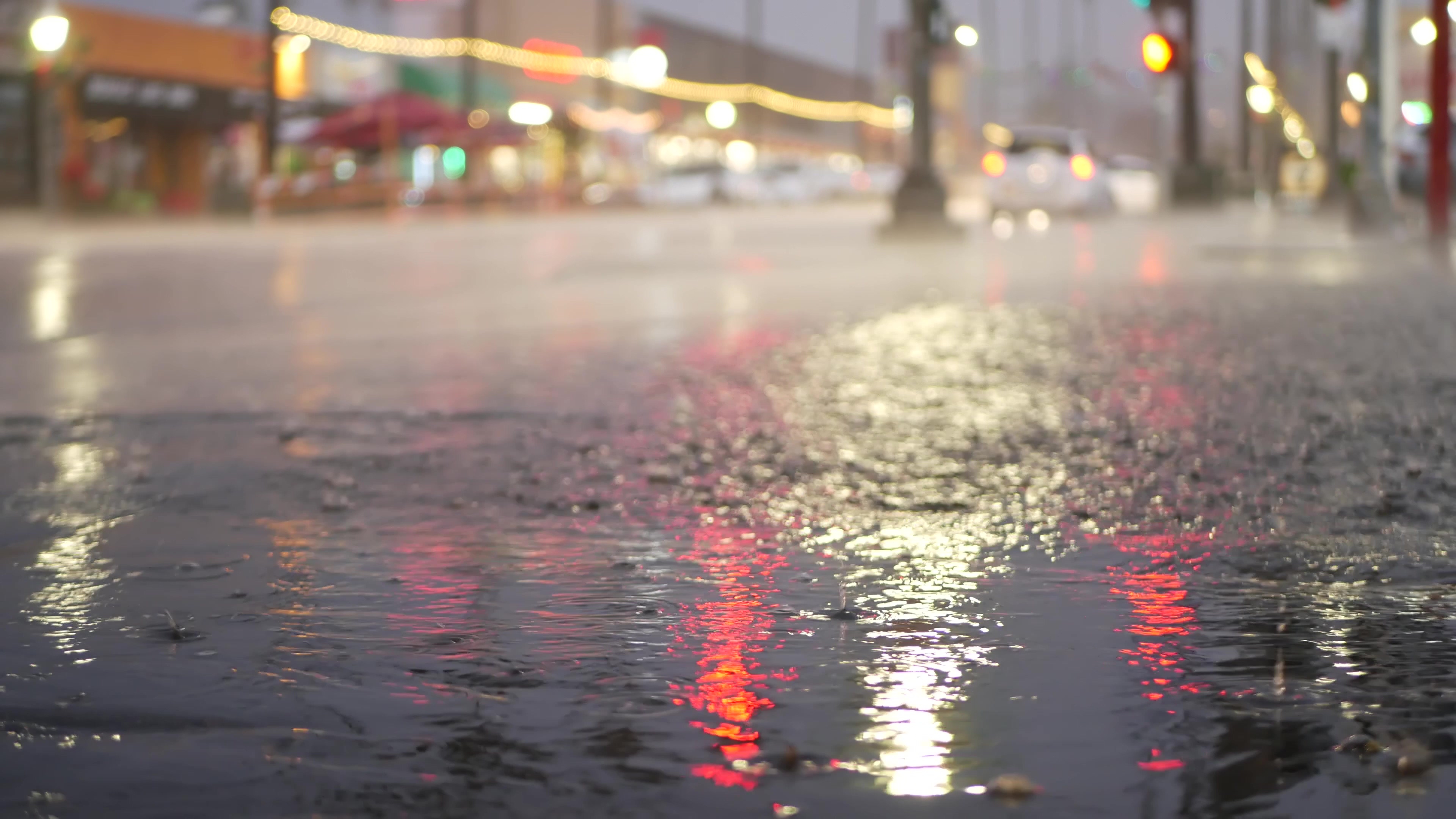 Cars lights reflection on road in rainy weather. Rain drops on wet asphalt of city street in USA, raindrops falling on sidewalk. Puddle of water on pavement. Torrential downpour or rainfall at night.