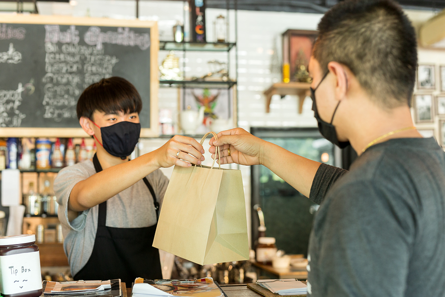 Social distance conceptual waiter giving takeaway bag to customer at cafe.