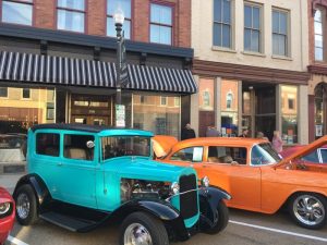 An orange vehicle and a blue vintage vehicle on a historic downtown street