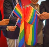 diverse group of business people (man, woman, gay, transgender, lesbian, asian, caucasian, african american, lgbtq) with rainbow flag on hand combine together as teamwork in office, selective focused