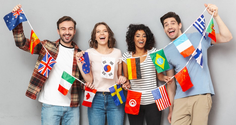 Image of happy group of friends standing isolated over grey wall background looking camera holding a lot of international flags.