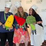 Three women wearing chef's hats and holding vegetable stuffies