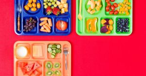 three lunch trays featuring fruits and vegetables sitting on a red background