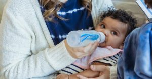 baby drinking from bottle gazes at camera from woman's arms