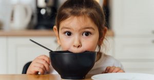 A child leans forward over an empty bowl gazing directly forward