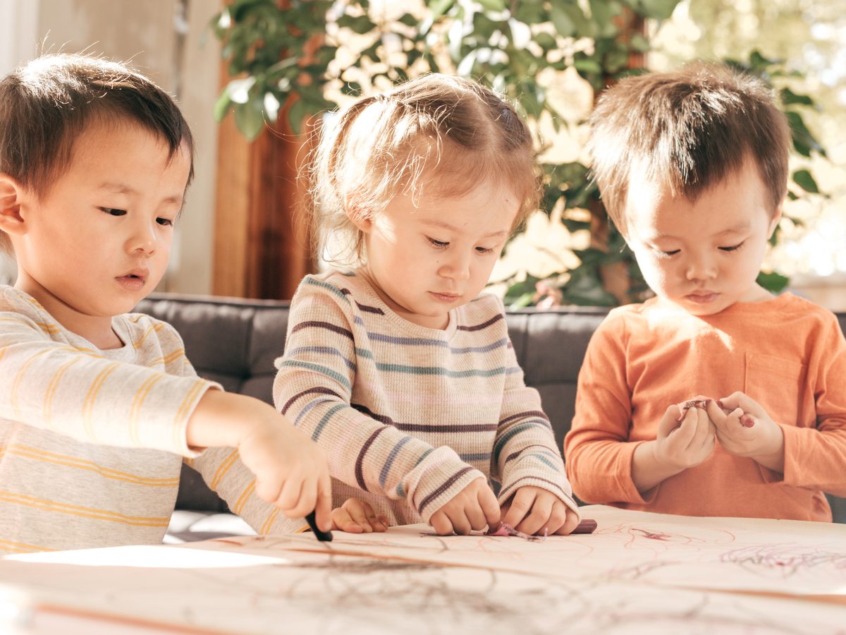 Three children sit side by side at a table working on CACFP Holiday activity pages