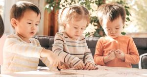 Three children sit side by side at a table working on CACFP Holiday activity pages