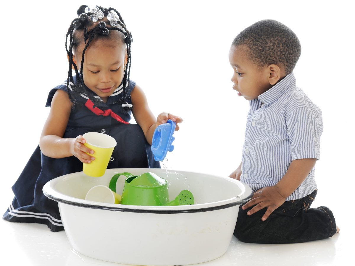 Two children playing sink or float with a bucket of water and toys