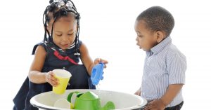 Two children play sink or float with toys in a bucket of water