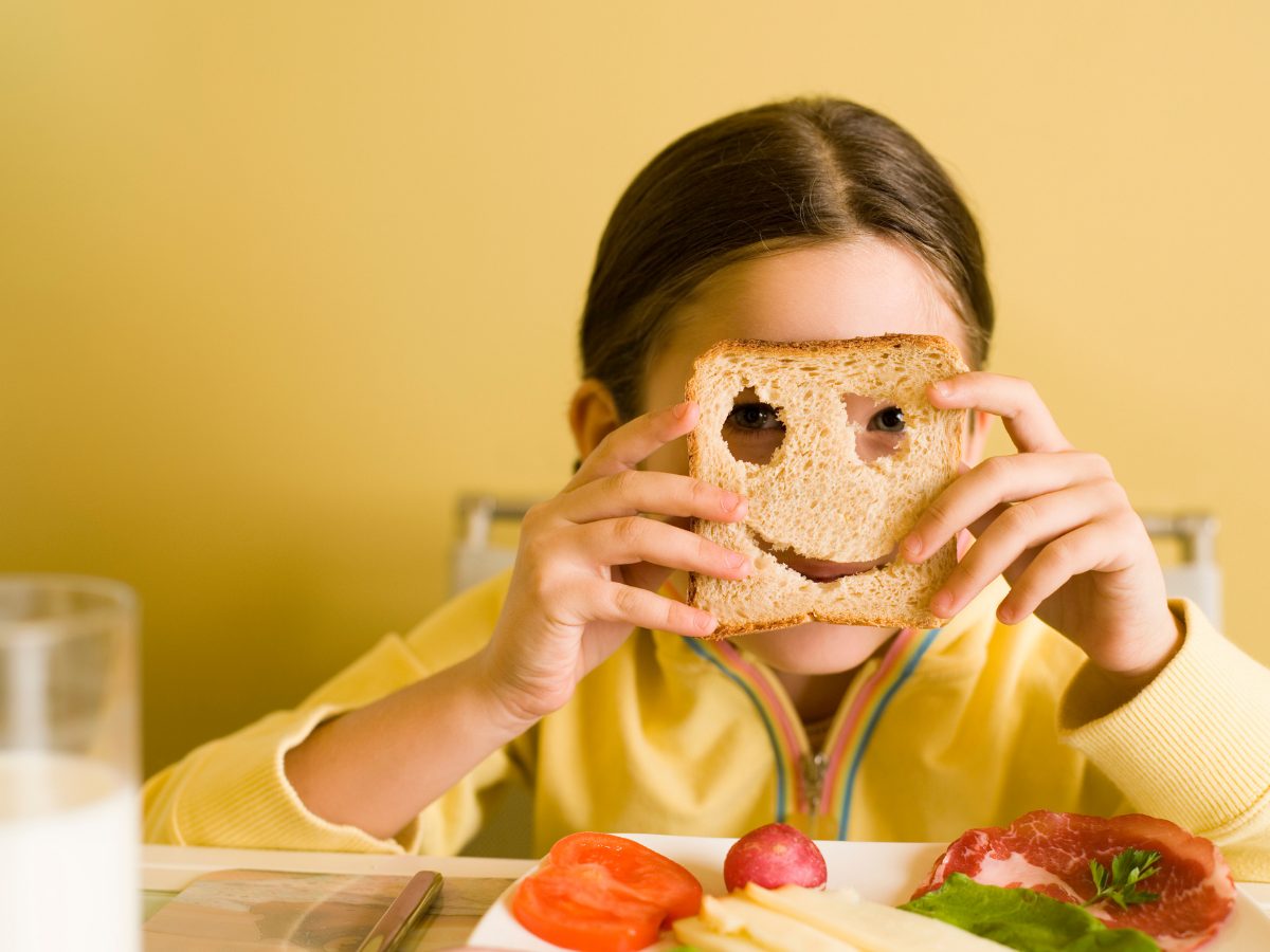 A CACFP participant in yellow holds a whole wheat piece of bread in front of her face
