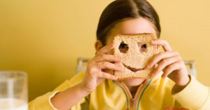 a CACFP participant in yellow holds a whole wheat piece of bread in front of her face