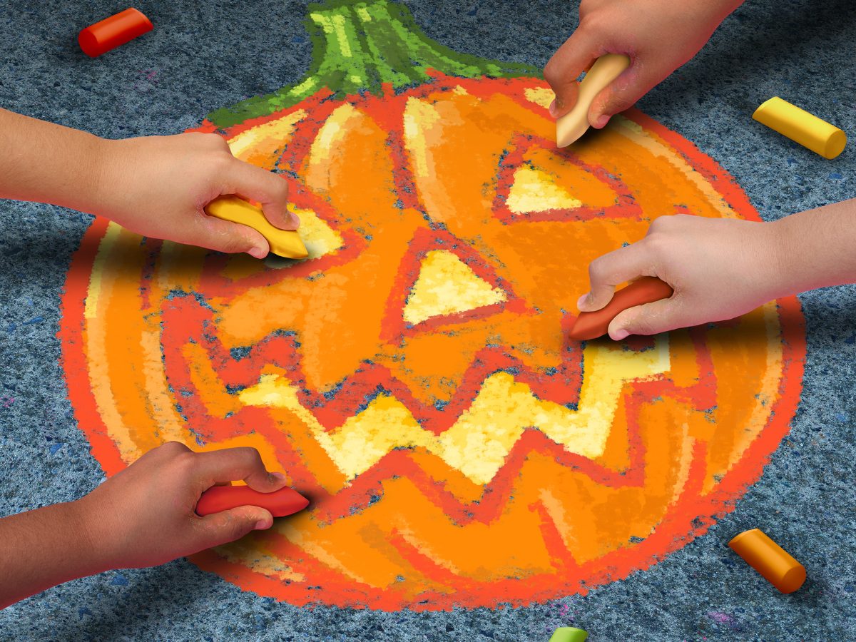 Children's hands chalk in an orange and yellow pumpkin on concrete