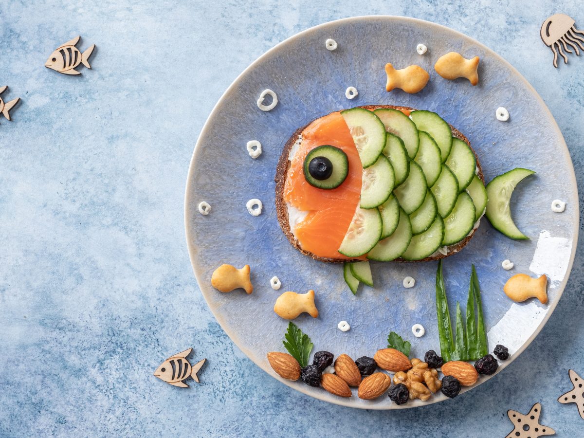 A plate with salmon toast. The salmon is arranged with sliced cucumbers to look like a fish.