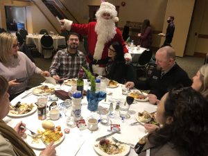 Santa and group of people around table with food
