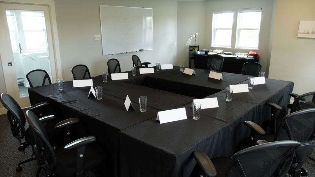 A photo of the DCC meeting room space which shows a South-West facing view of the room, with tables set up in a square configuration to accommodate 10 guests and a table with food.