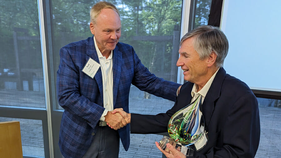 NCBIO Chairman Neal Fowler shakes the hand of John Wagner who is holding an award.