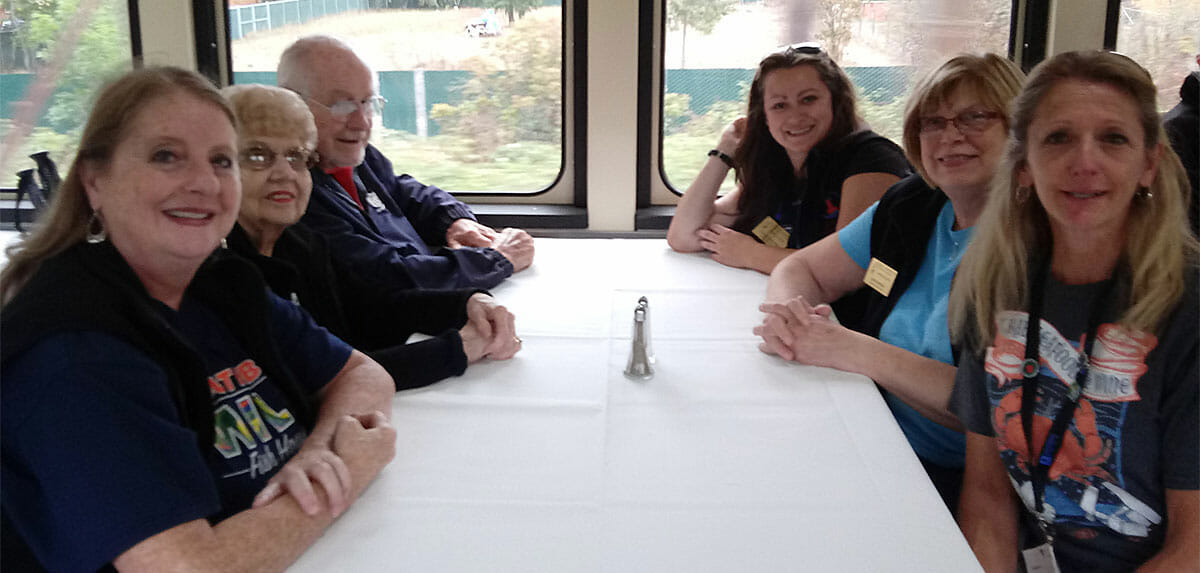 Six people sitting at a table near windows on a train.
