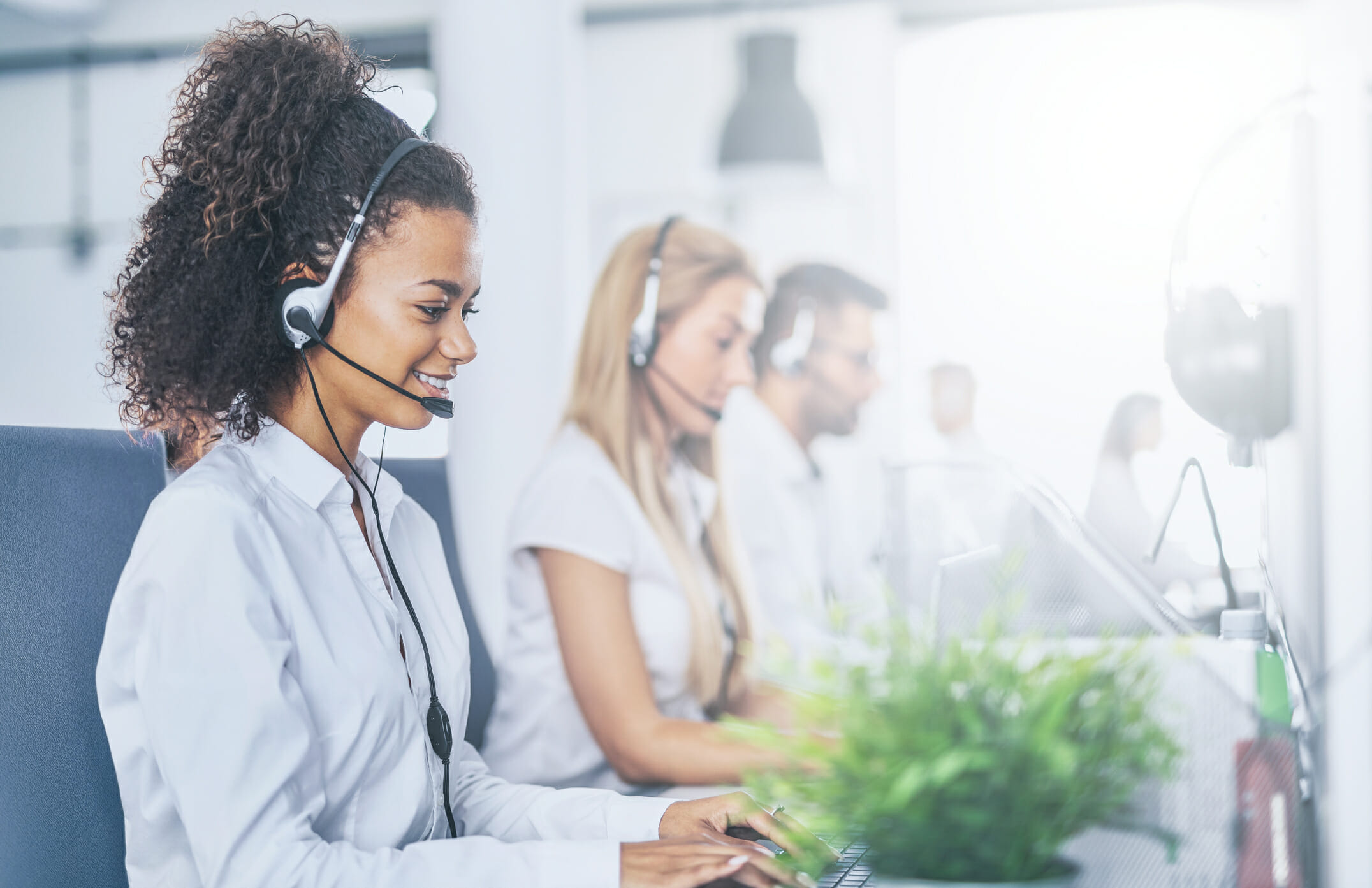 Call center worker accompanied by her team. Smiling customer support operator at work. Young employee working with a headset.