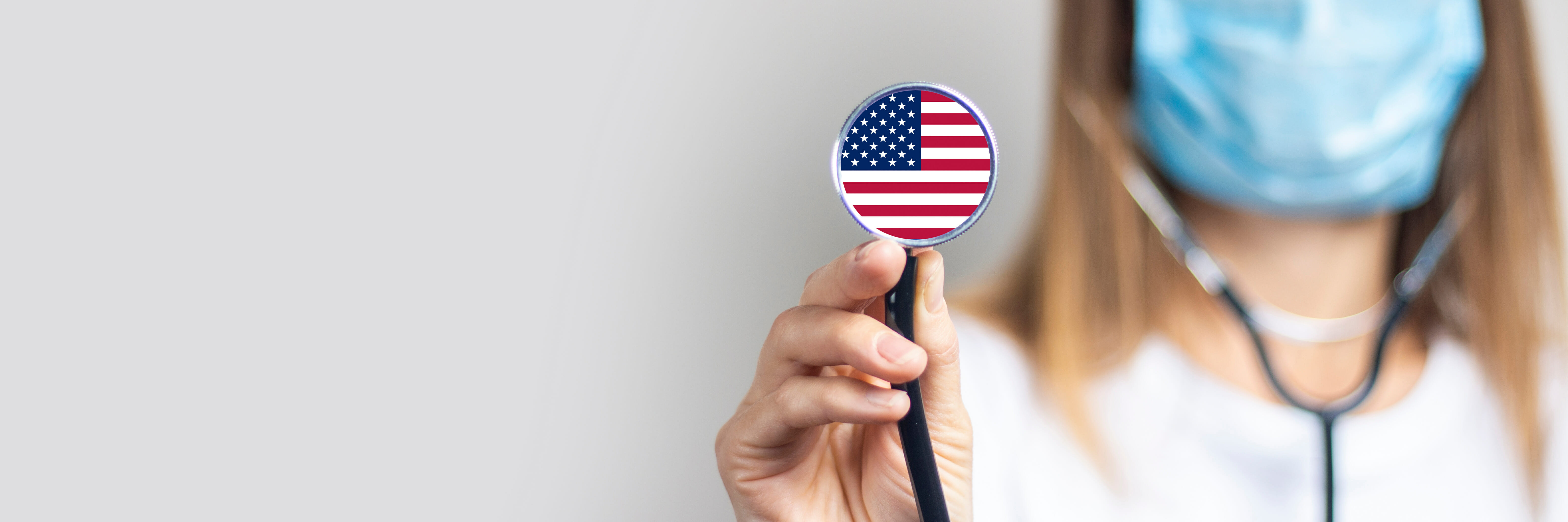 female doctor in a medical mask holds a stethoscope on a light background. Added flag of United States of America. Concept medicine, level of medicine, virus, epidemic. Baner female doctor in a medical mask holds a stethoscope on a light background. Added flag of United States of America. Concept medicine, level of medicine, virus, epidemic. Baner.