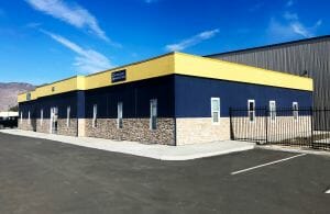 A side view of a one story office building with yellow and blue paint and stone siding in a parking lot