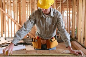 A man working building a home and measuring some wood