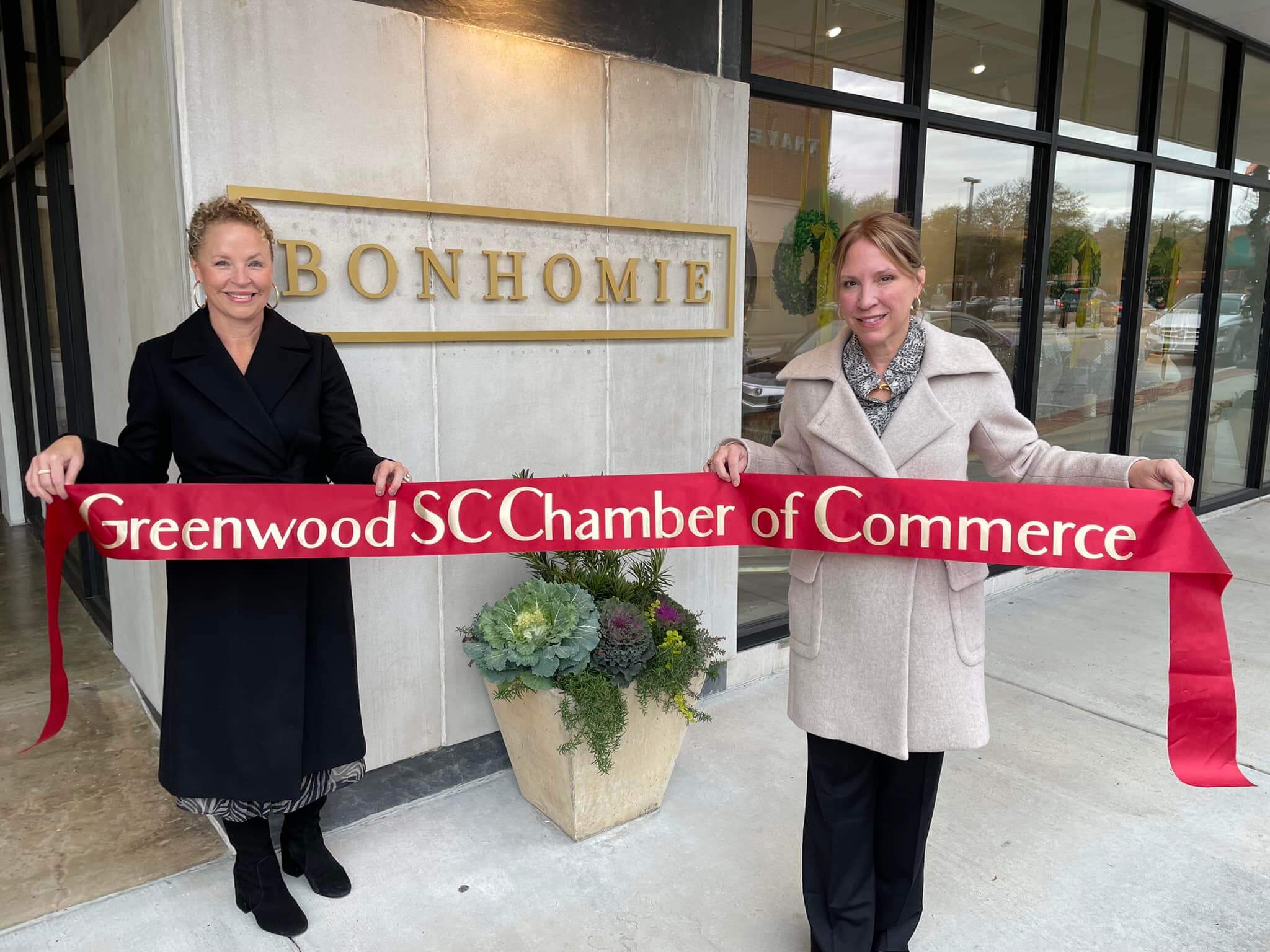two women holding a ribbon with greenwood sc chamber of commerce on it