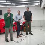 3 people on stage in front of sports car
