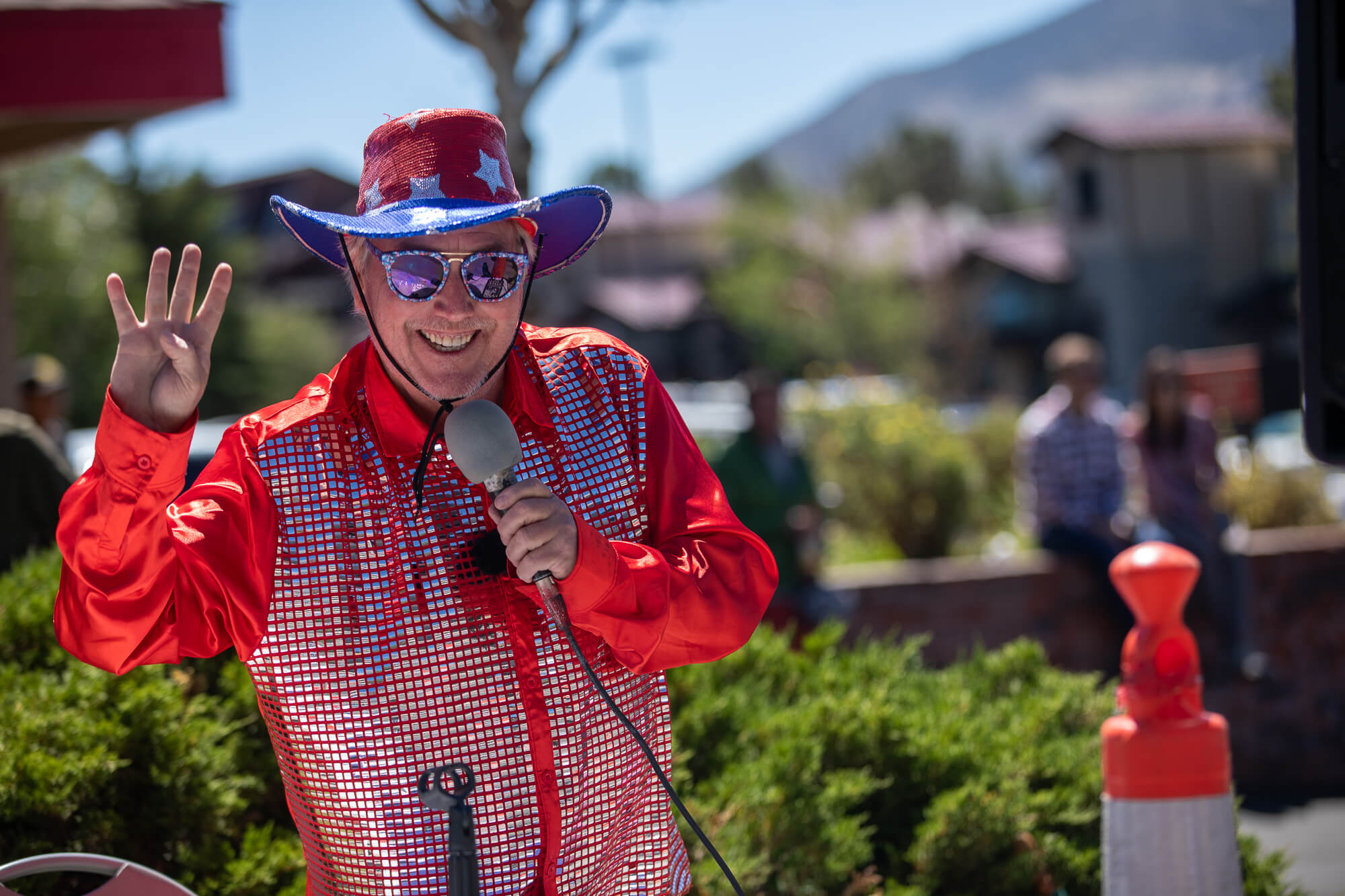 A 4th of July parade announcer dressed in a shiny American flag hat and a sequined red button down shirt