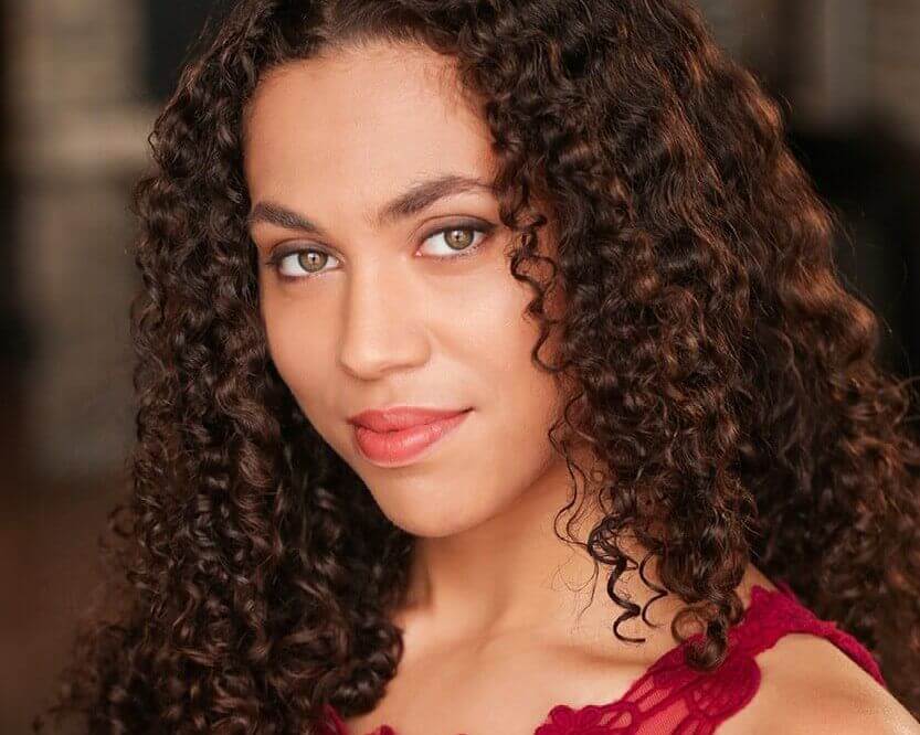 Headshot of Aidaa Peerzada. A medium skinned woman with medium length curly brown hair and hazel eyes. She is wearing a red lace tank top.