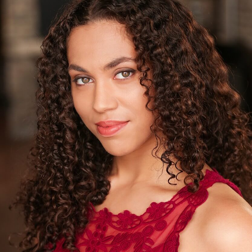 Headshot of Aidaa Peerzada. A medium skinned woman with medium length curly brown hair and hazel eyes. She is wearing a red lace tank top. 