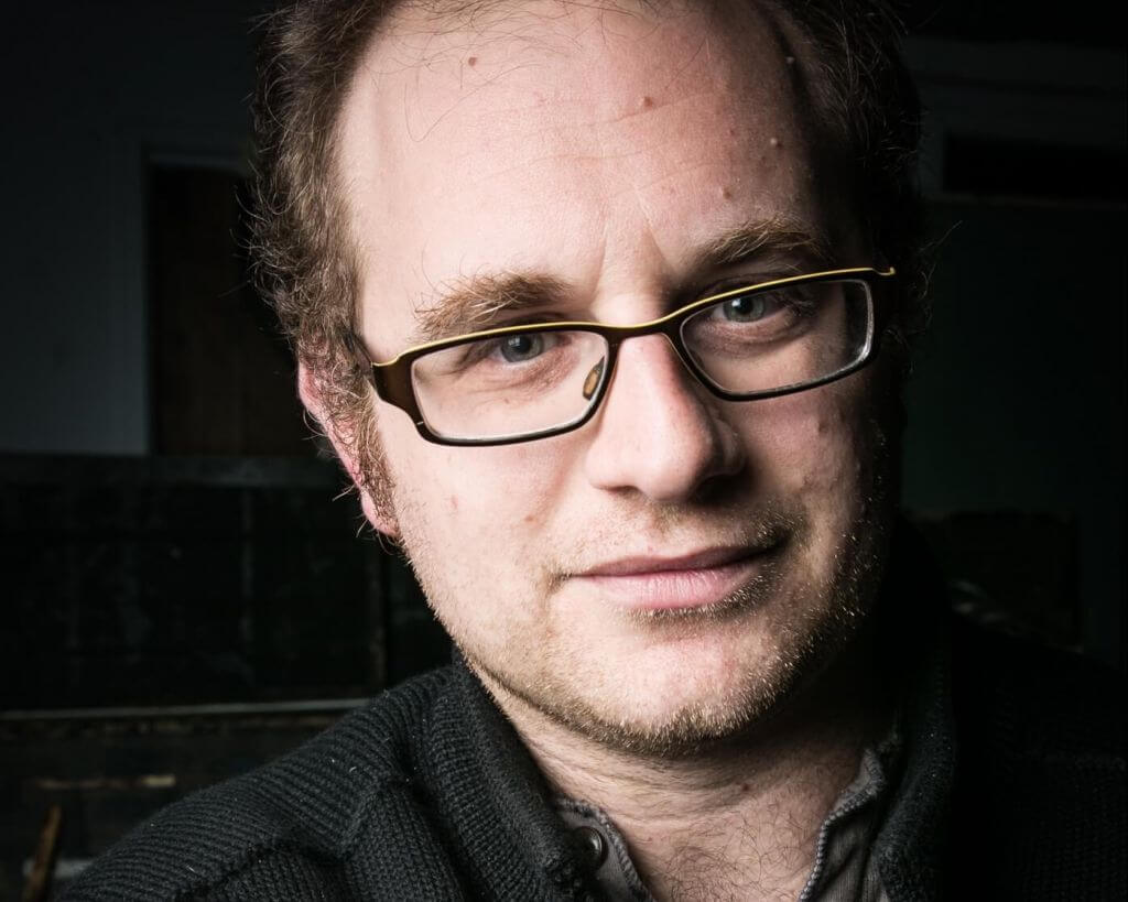 A white partially balding human with glasses looking into the camera