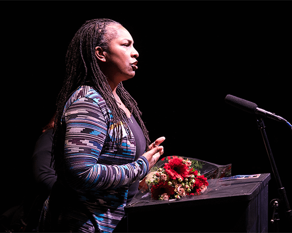 Kimberly Ridgeway, a Black woman with her hair in braids, speaks into a microphone.