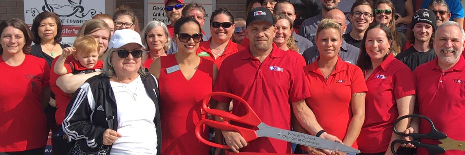 People in red shirts posing with ribbon cutting scissors