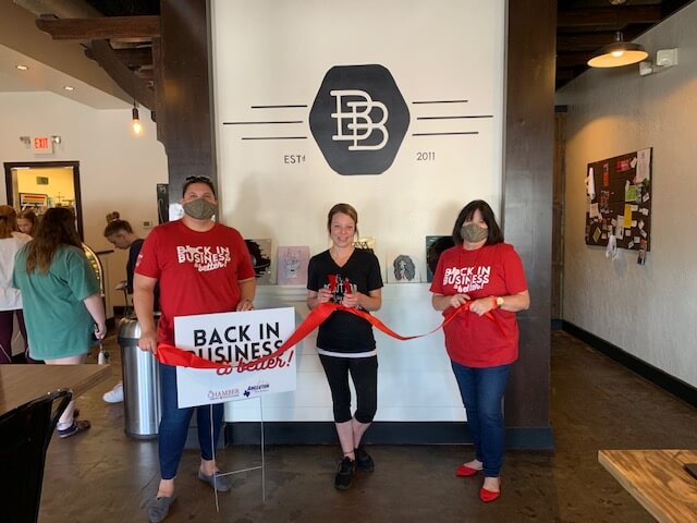 3 people holding back in business sign ribbon cutting