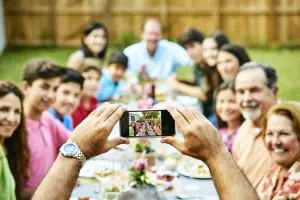 Hands of man photographing multi-generation family Hands of man photographing family sitting at dining table. Multi-generation family is enjoying garden party. They are celebrating at back yard.