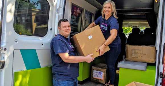 2 adult volunteers lifting cardboard boxed out of van